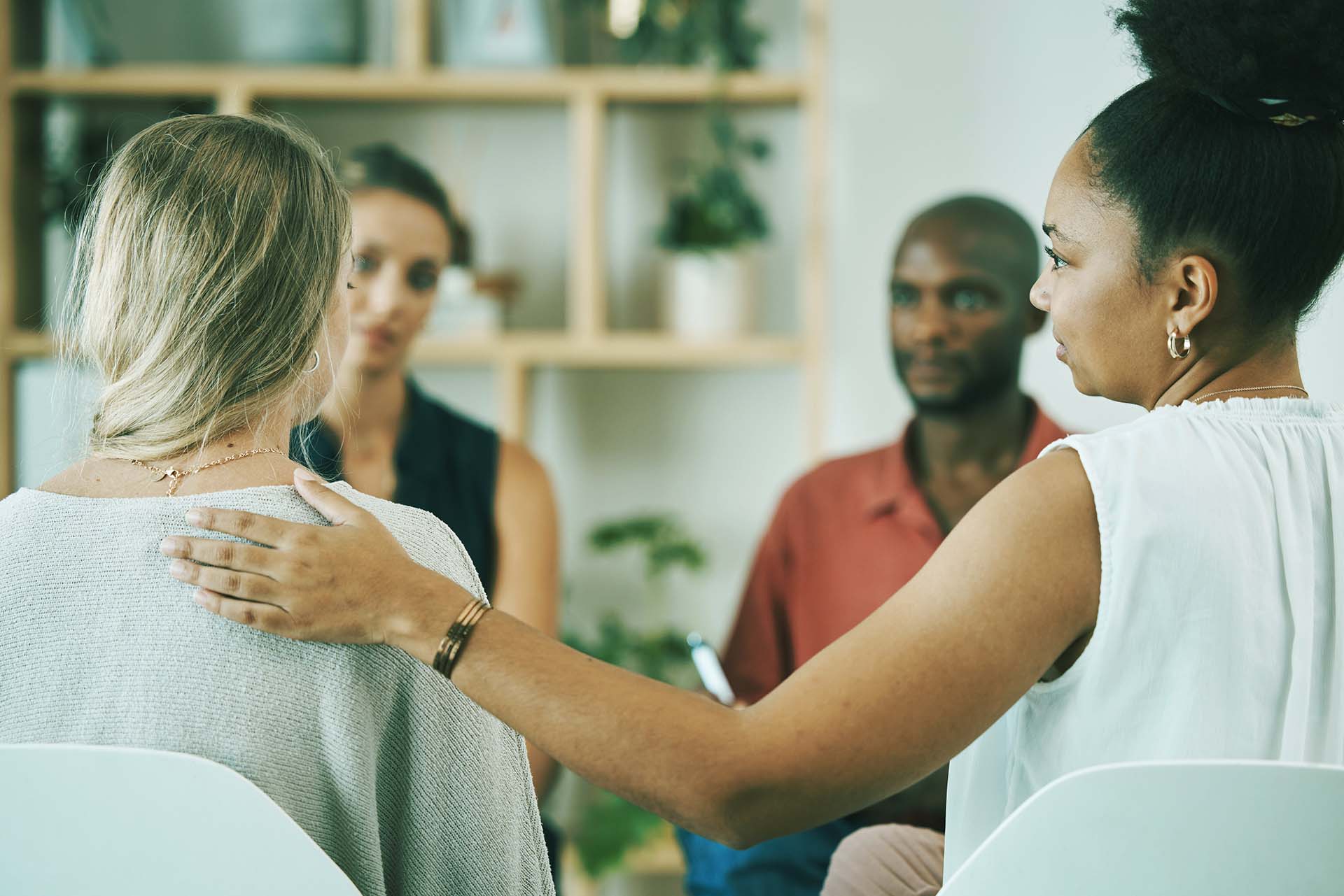 Image of 4 group members sitting in a circle. A Black woman is placing her hand comfortingly on the shoulder of a blonde woman whose back is to the camera. Kings View Behavioral Health Systems was founded to address the need for mental health, drug, and alcohol treatment.